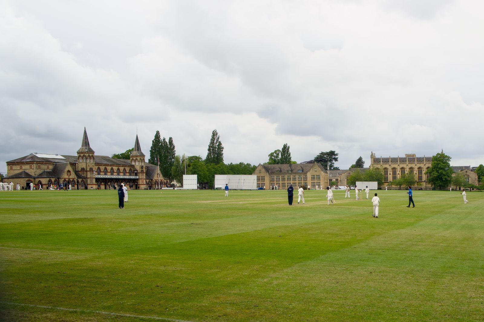 A cricket match on a green ground in front of a historic pavilion